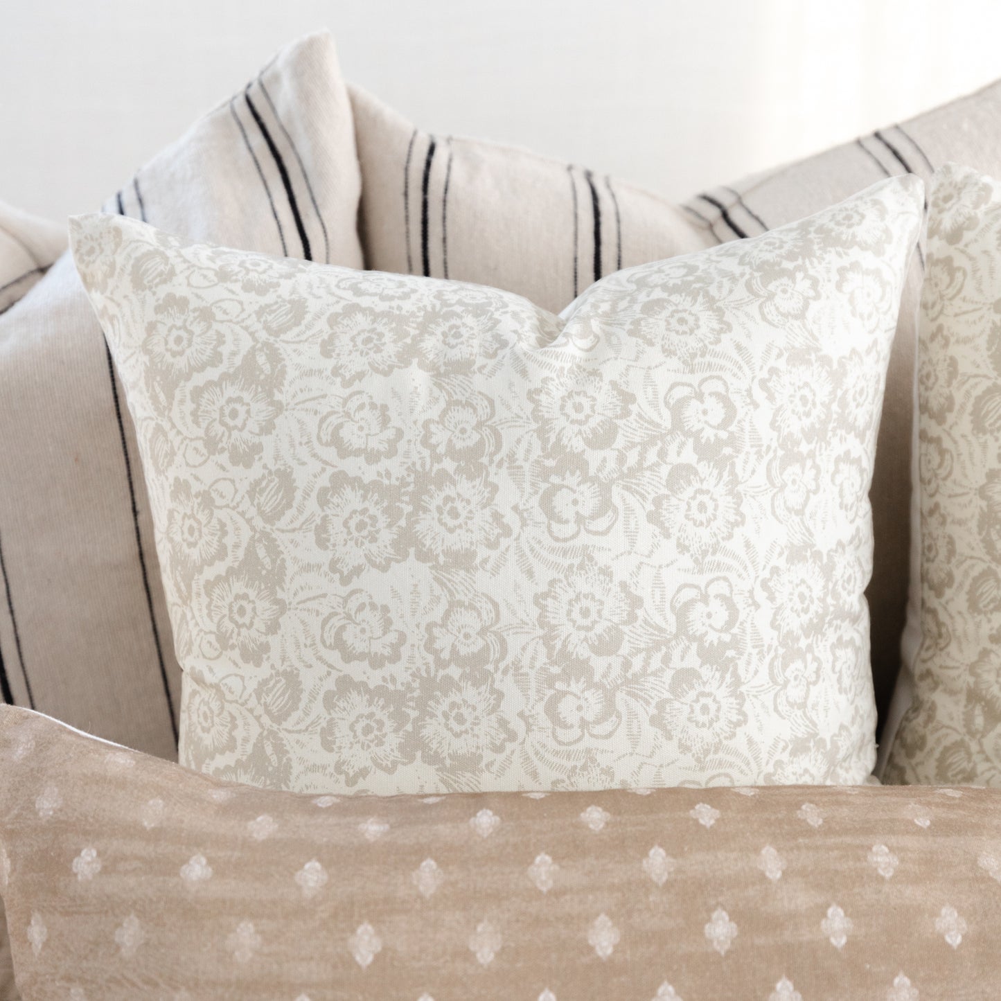 Cream lumbar pillow with damask floral pattern displayed with coordinating striped and dotted accent pillows.