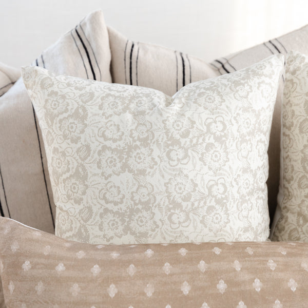 Cream lumbar pillow with damask floral pattern displayed with coordinating striped and dotted accent pillows.