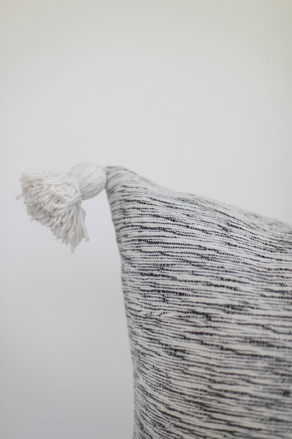Decorative pillow with horizontal striped pattern in gray and white, featuring a white twisted tassel corner detail.
