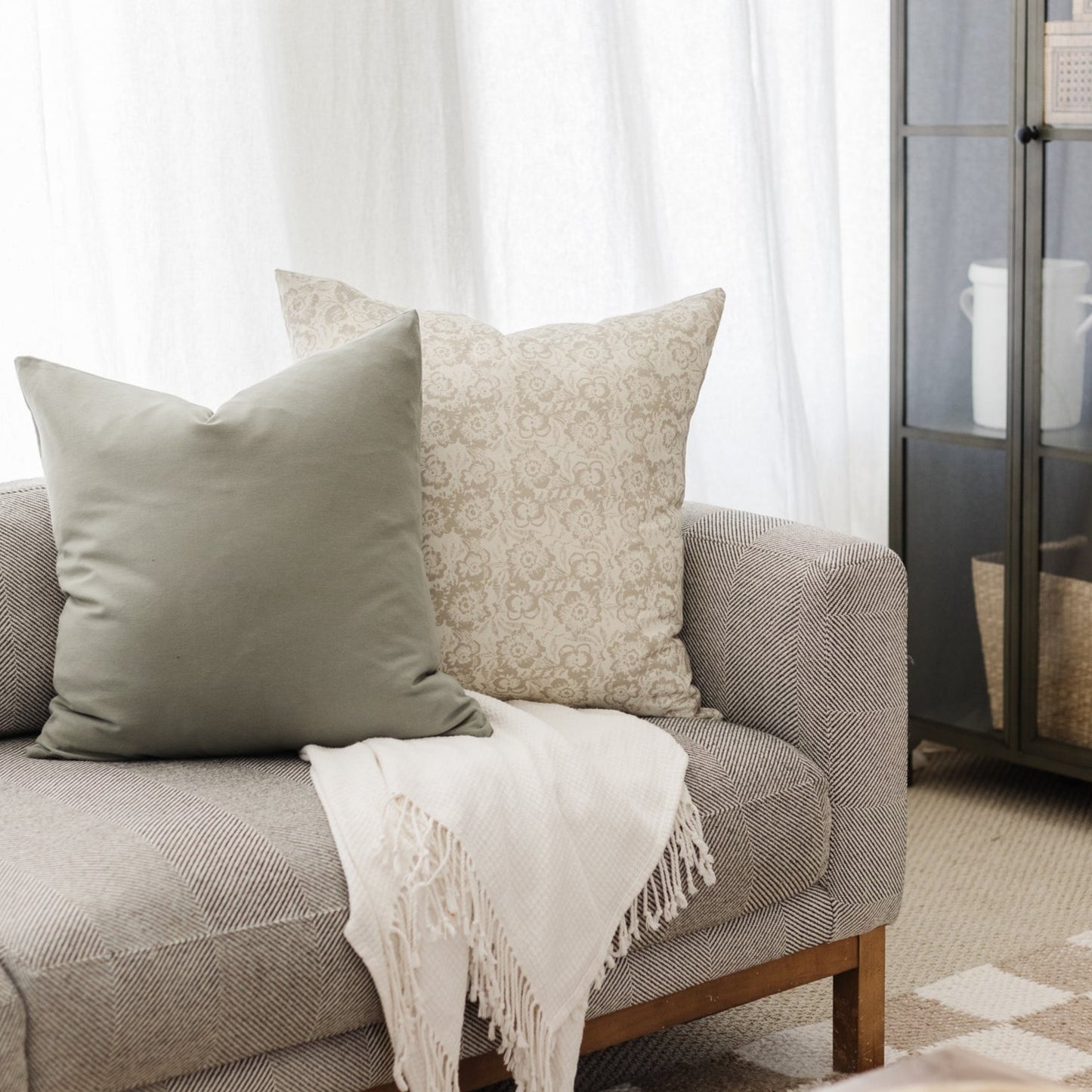 Solid sage green pillow cover and patterned beige damask pillow cover displayed on gray upholstered chair.