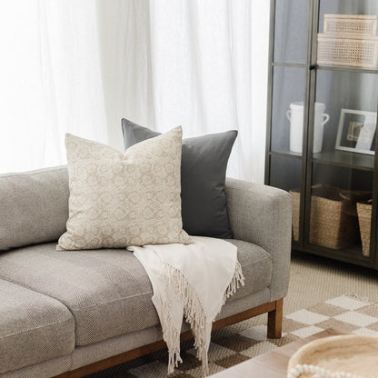 Beige patterned pillow cover and charcoal solid pillow cover displayed on a gray upholstered sofa.