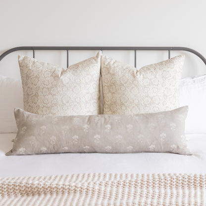 Three beige pillow covers with floral damask and botanical patterns arranged on a bed with metal headboard.
