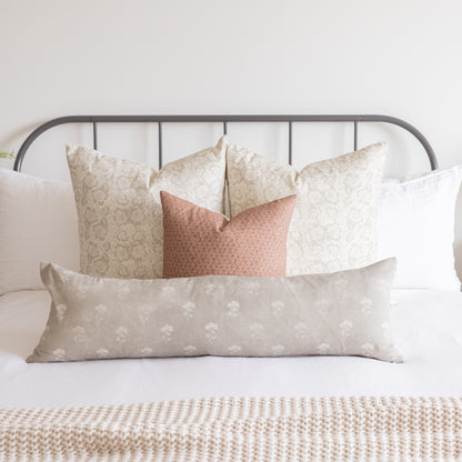 Beige and terracotta patterned pillow covers arranged on a bed with an iron headboard.