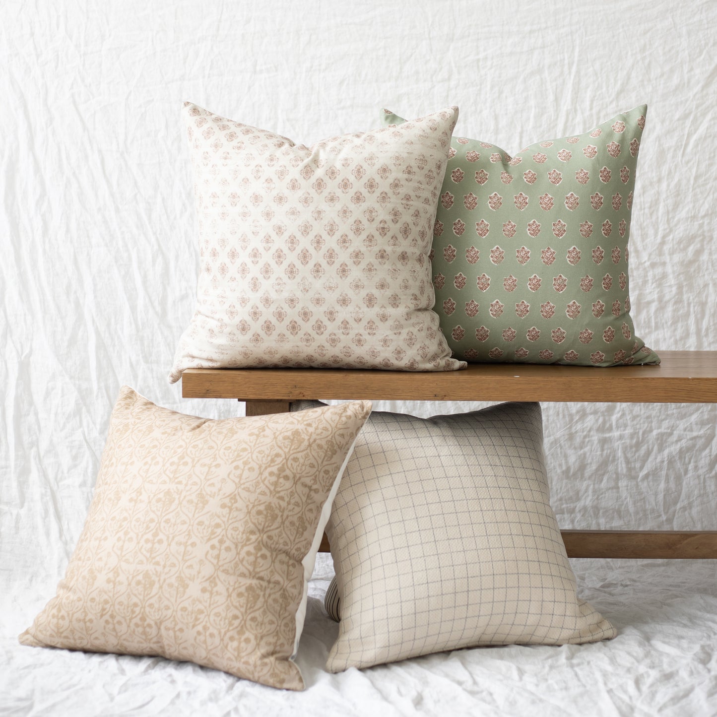 Four decorative pillows in various neutral and sage patterns displayed on wooden shelves.