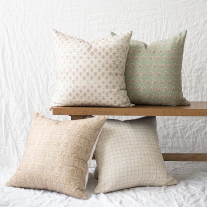 Four decorative pillows in various neutral and sage patterns displayed on wooden shelves.