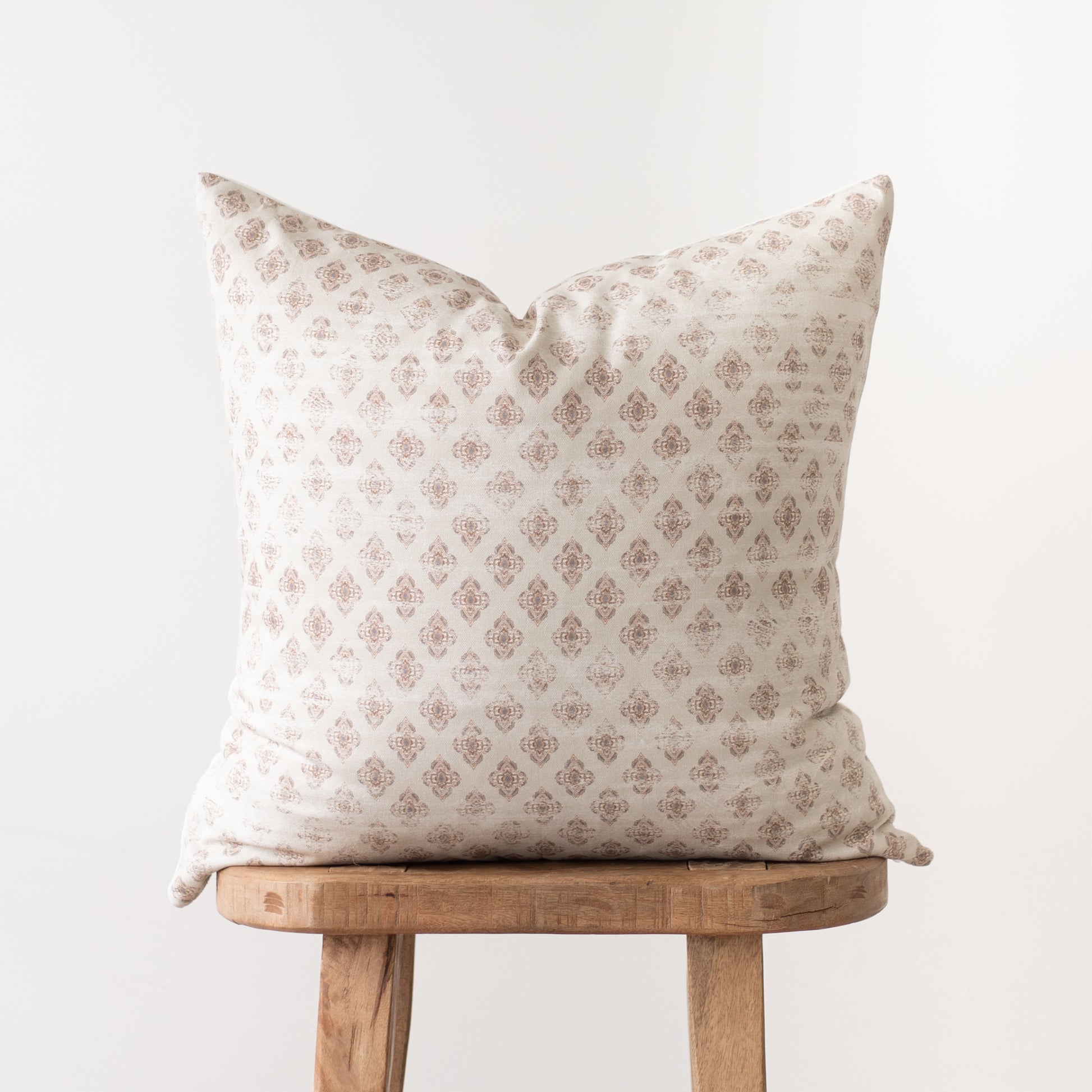 Cream pillow cover with tan geometric diamond pattern, displayed on wooden stool.