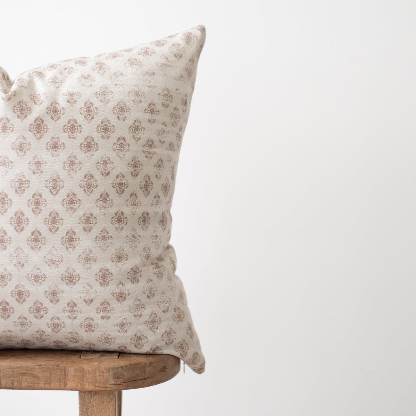 Cream pillow with repeating tan damask pattern, displayed on wooden chair.