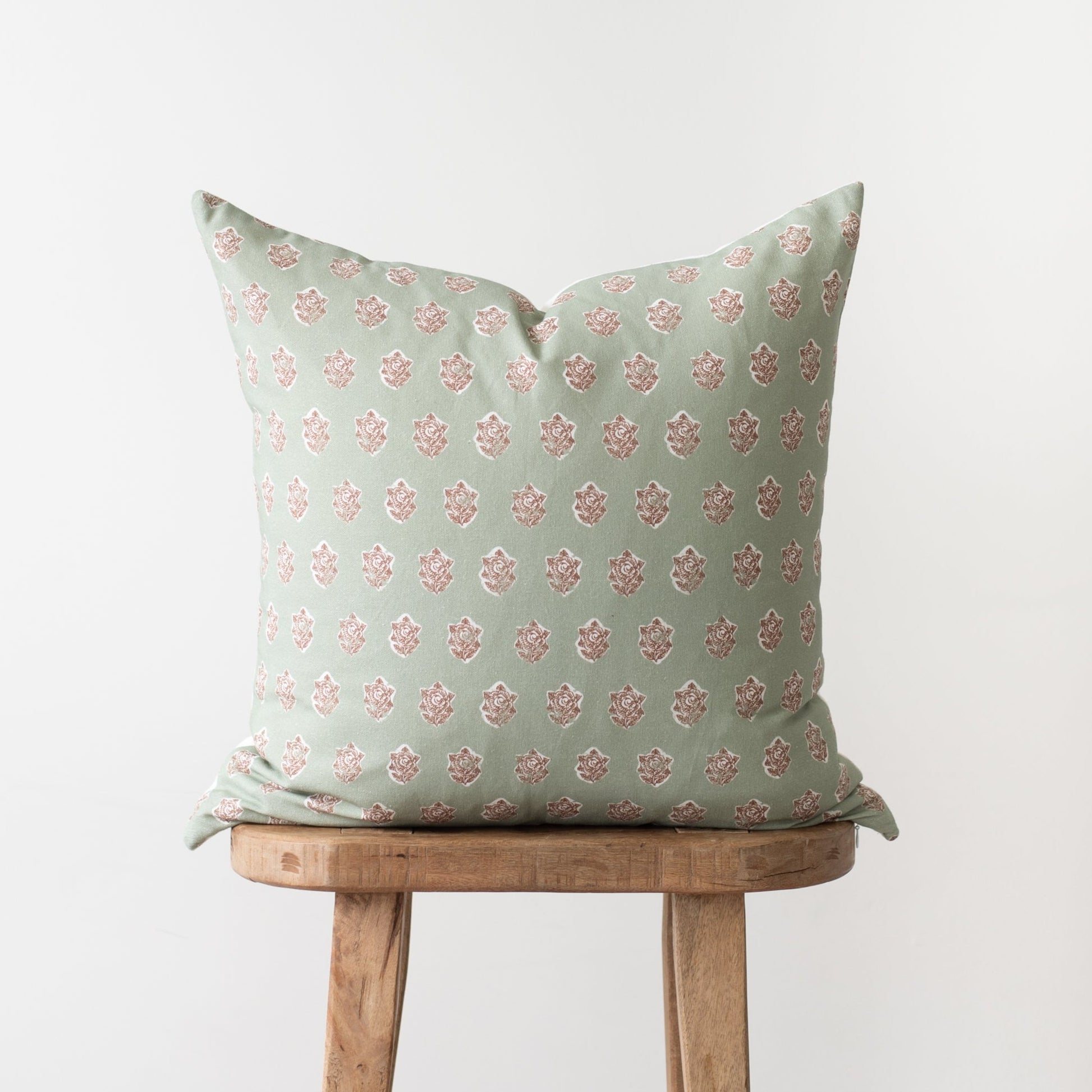 Sage green pillow with pink damask pattern, displayed on wooden chair.