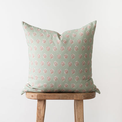 Sage green pillow with pink damask pattern, displayed on wooden chair.