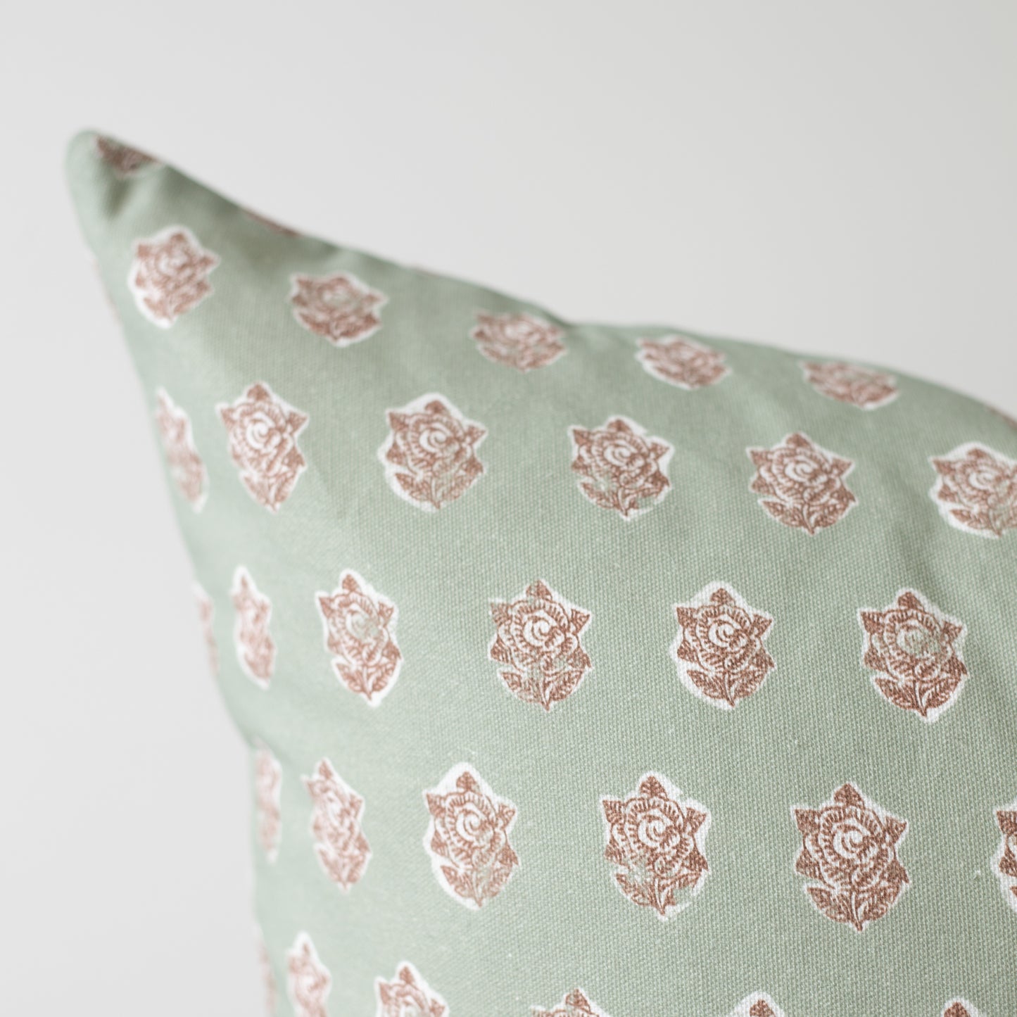 Sage green pillow with repeating rose gold floral medallion pattern.