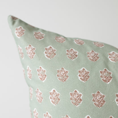 Sage green pillow with repeating rose gold floral medallion pattern.