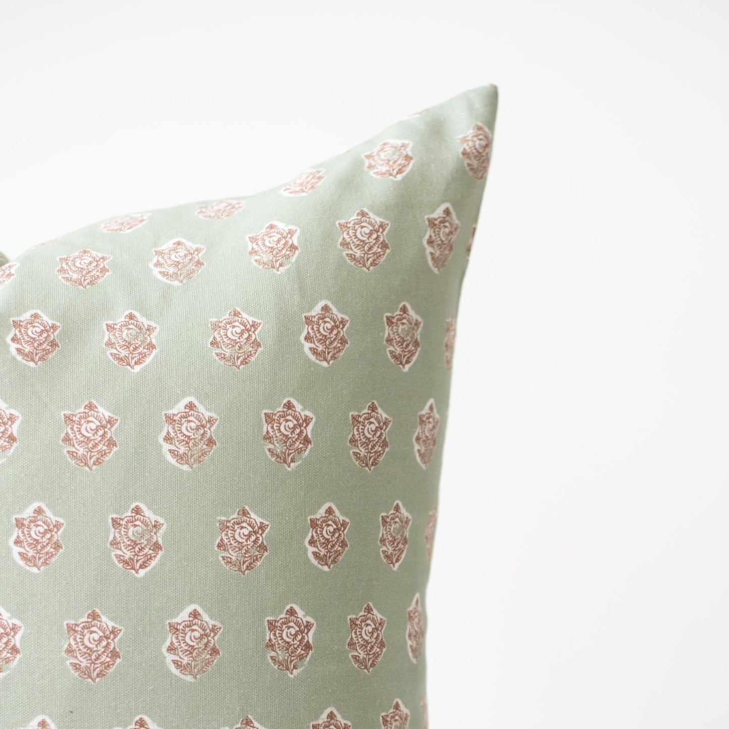 Light green pillow with repeating rose print in dusty pink throughout.