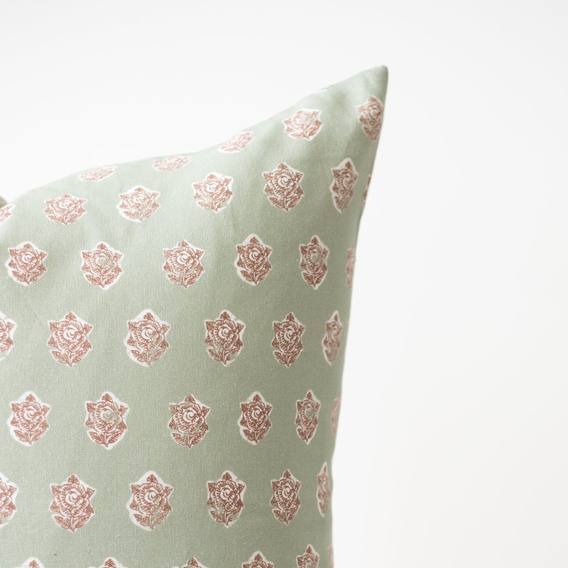 Light green pillow with repeating rose print in dusty pink throughout.