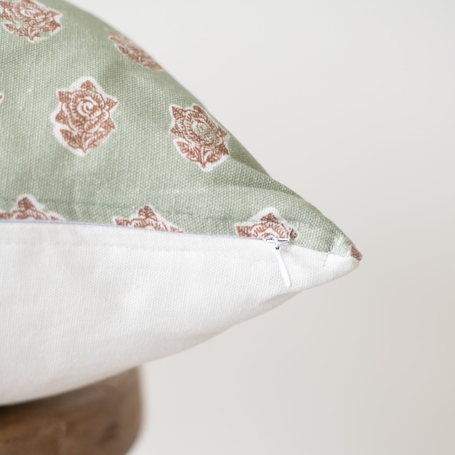 Sage green pillow with rust floral pattern and white zipper closure on side.