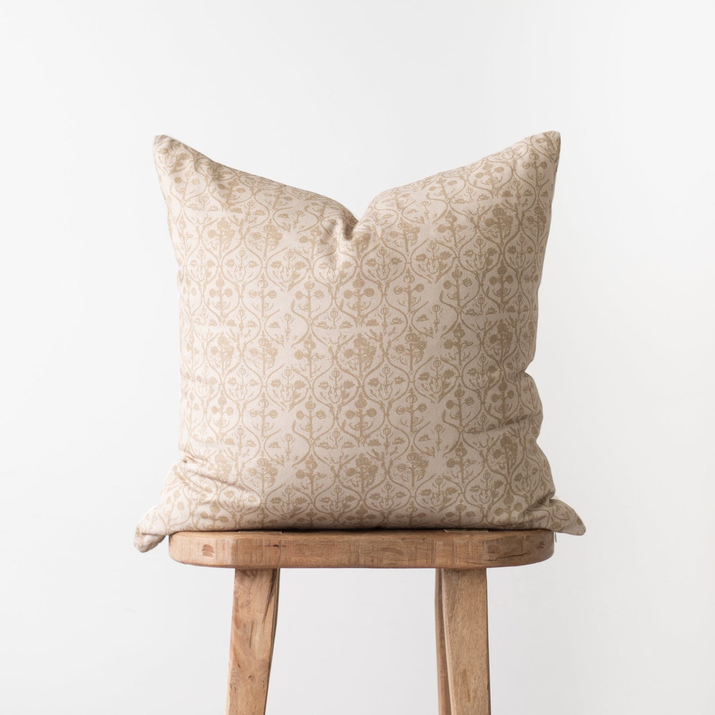 Cream and beige damask patterned pillow displayed on a wooden stool.