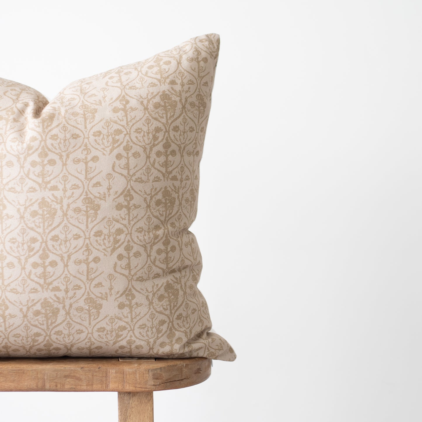 Beige and cream damask patterned pillow with geometric floral design resting on wooden stand.