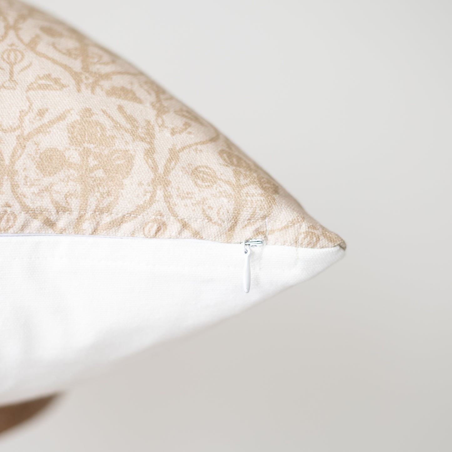 Rectangular pillow with beige damask pattern on top and white base, showing zipper closure detail.