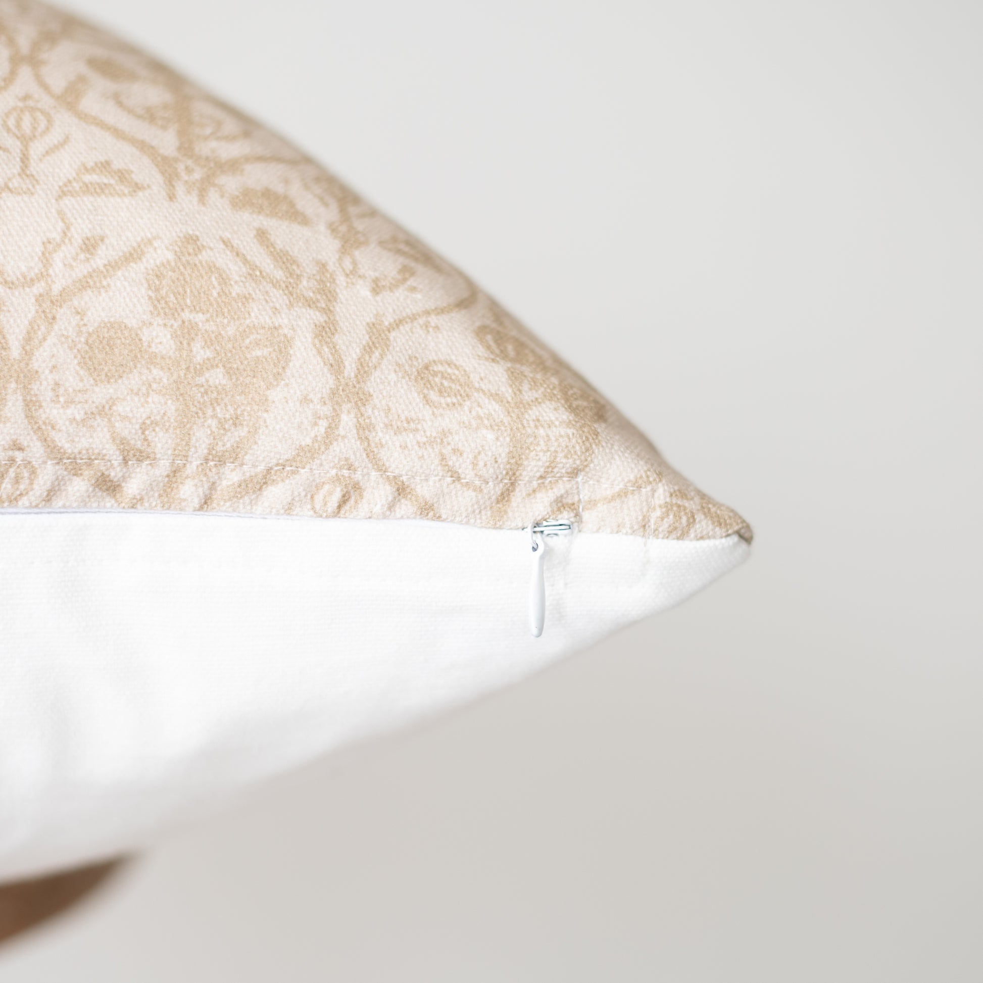 Rectangular pillow with beige damask pattern on top and white base, showing zipper closure detail.
