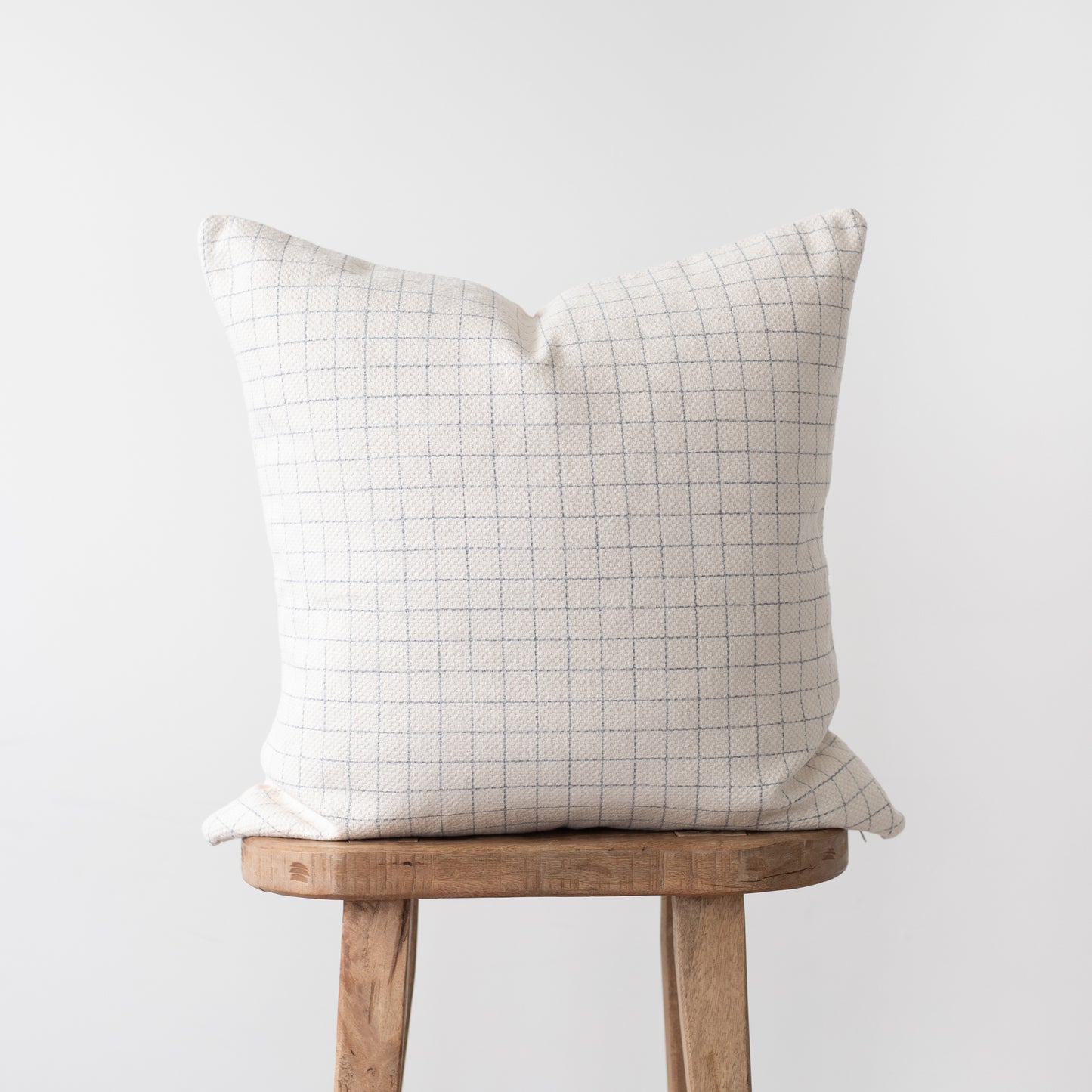 Cream pillow cover with gray grid pattern displayed on wooden stool.