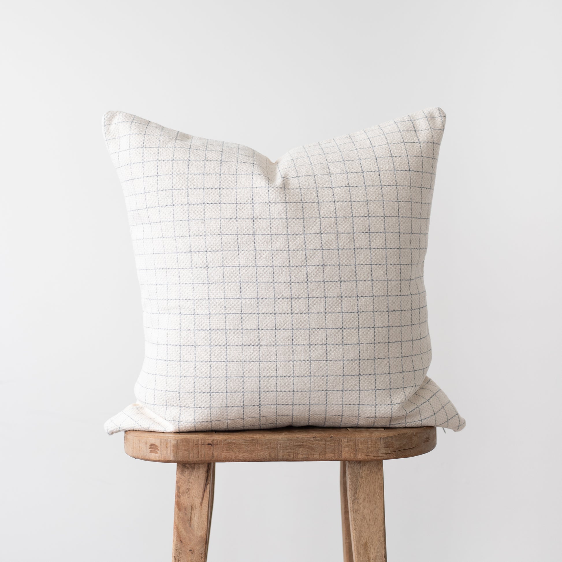 Cream pillow cover with gray grid pattern displayed on wooden stool.