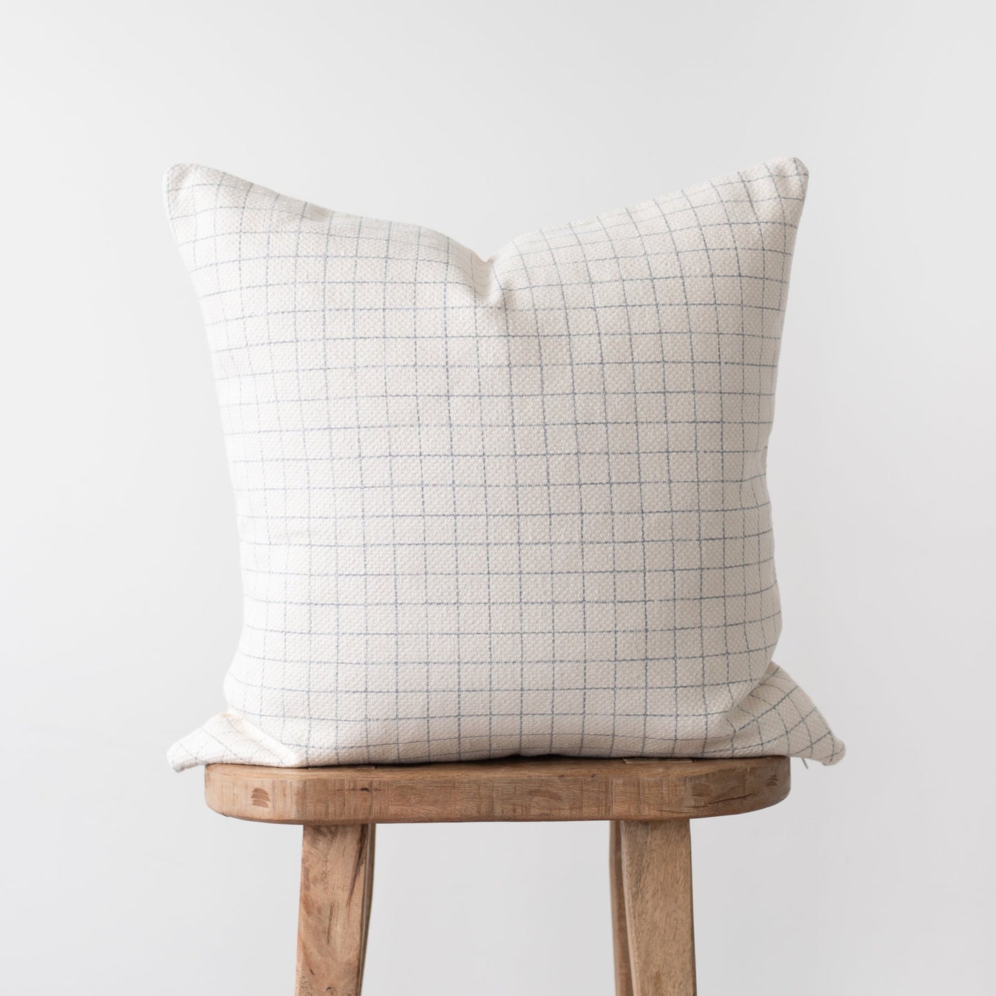 Cream throw pillow with taupe grid pattern displayed on wooden stool.
