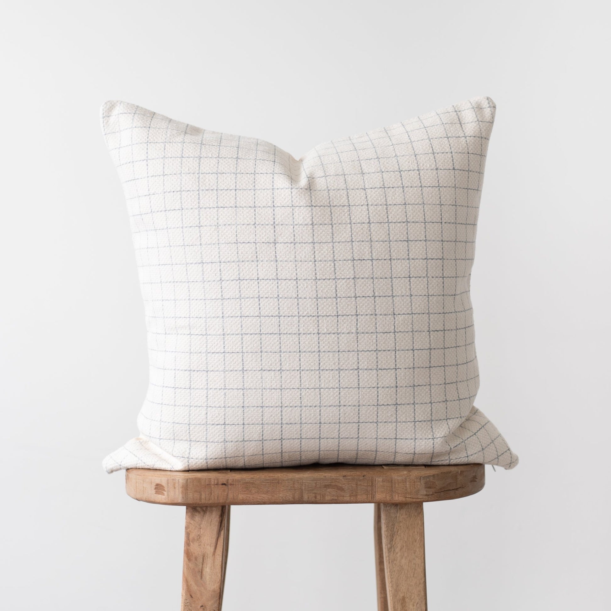 Cream throw pillow with taupe grid pattern displayed on wooden stool.