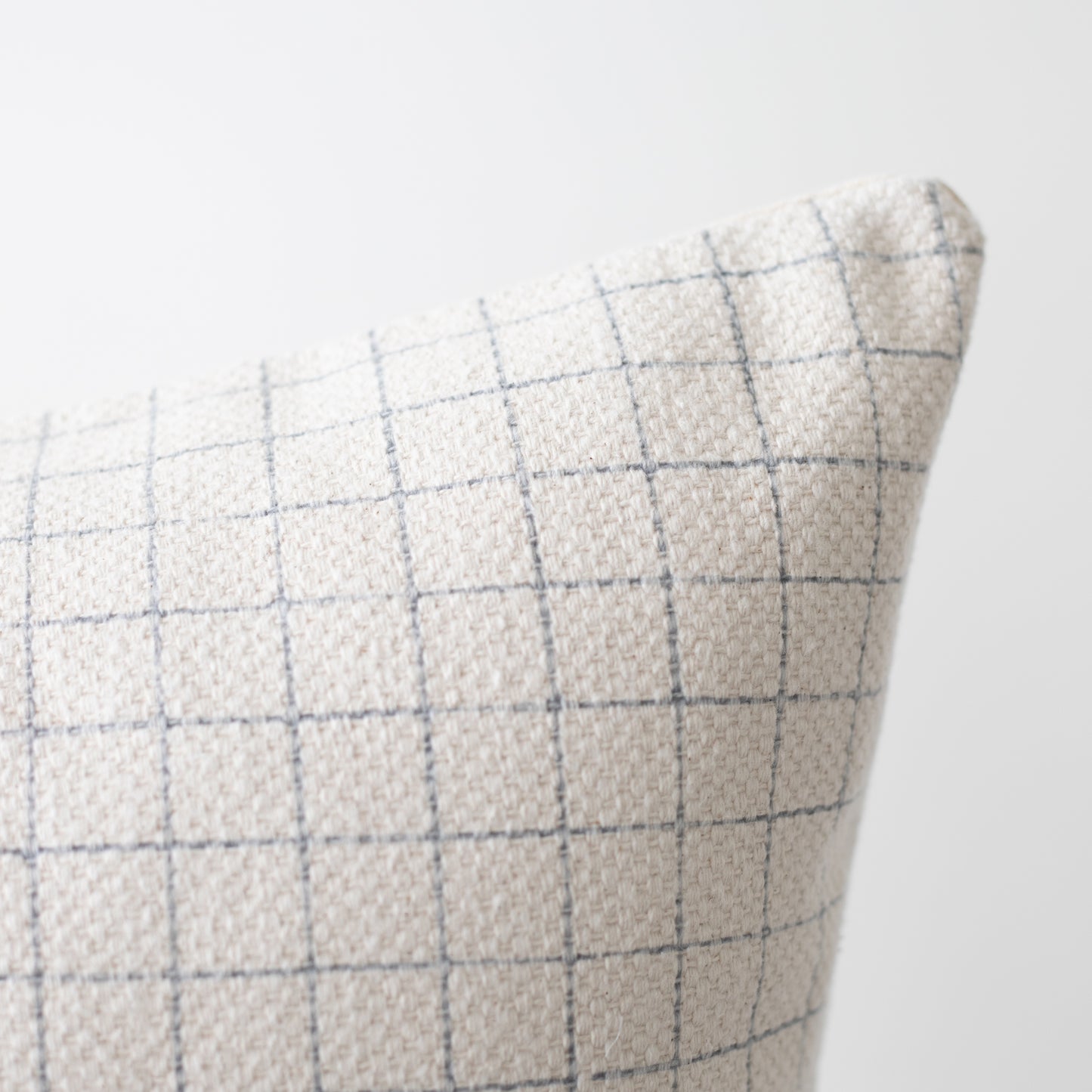 Beige linen pillow with blue grid pattern, shown at an angle displaying texture and weave detail.
