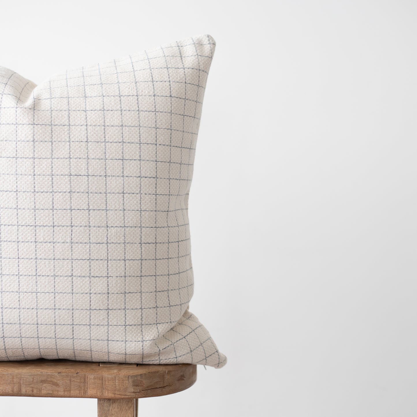 Cream pillow with gray grid pattern on wooden stool.