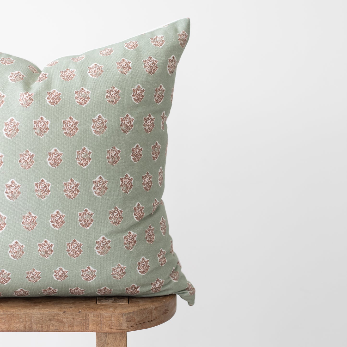 Sage green pillow with repeating rose medallion pattern in mauve, displayed on wooden chair.