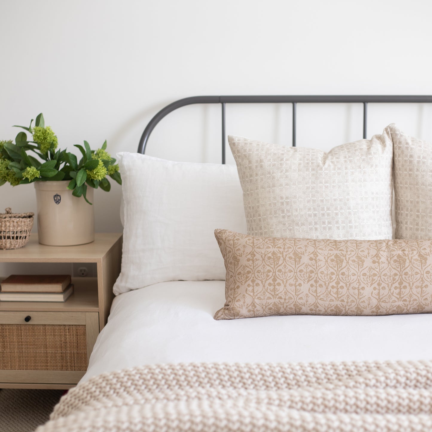Rectangular lumbar pillow with tan and cream floral geometric pattern displayed on a bed with coordinating pillows.