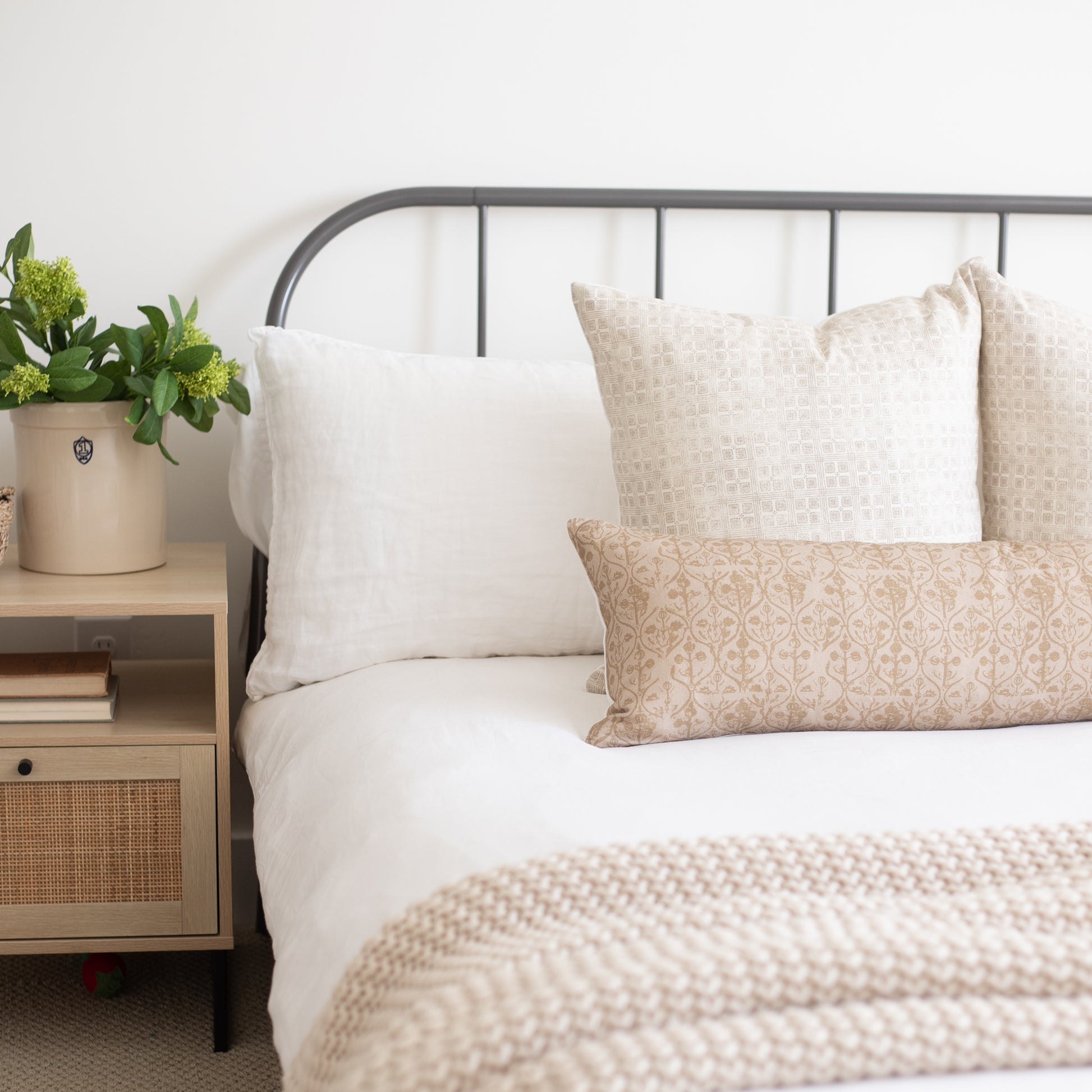 Rectangular throw pillow with beige hourglass floral pattern displayed on bed with white and patterned pillows.