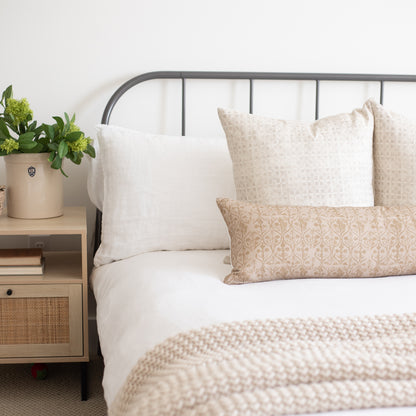 Rectangular throw pillow with beige hourglass floral pattern displayed on bed with white and patterned pillows.