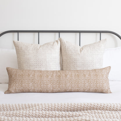 Three decorative pillows with geometric floral patterns in cream and tan tones arranged on a bed with metal headboard.