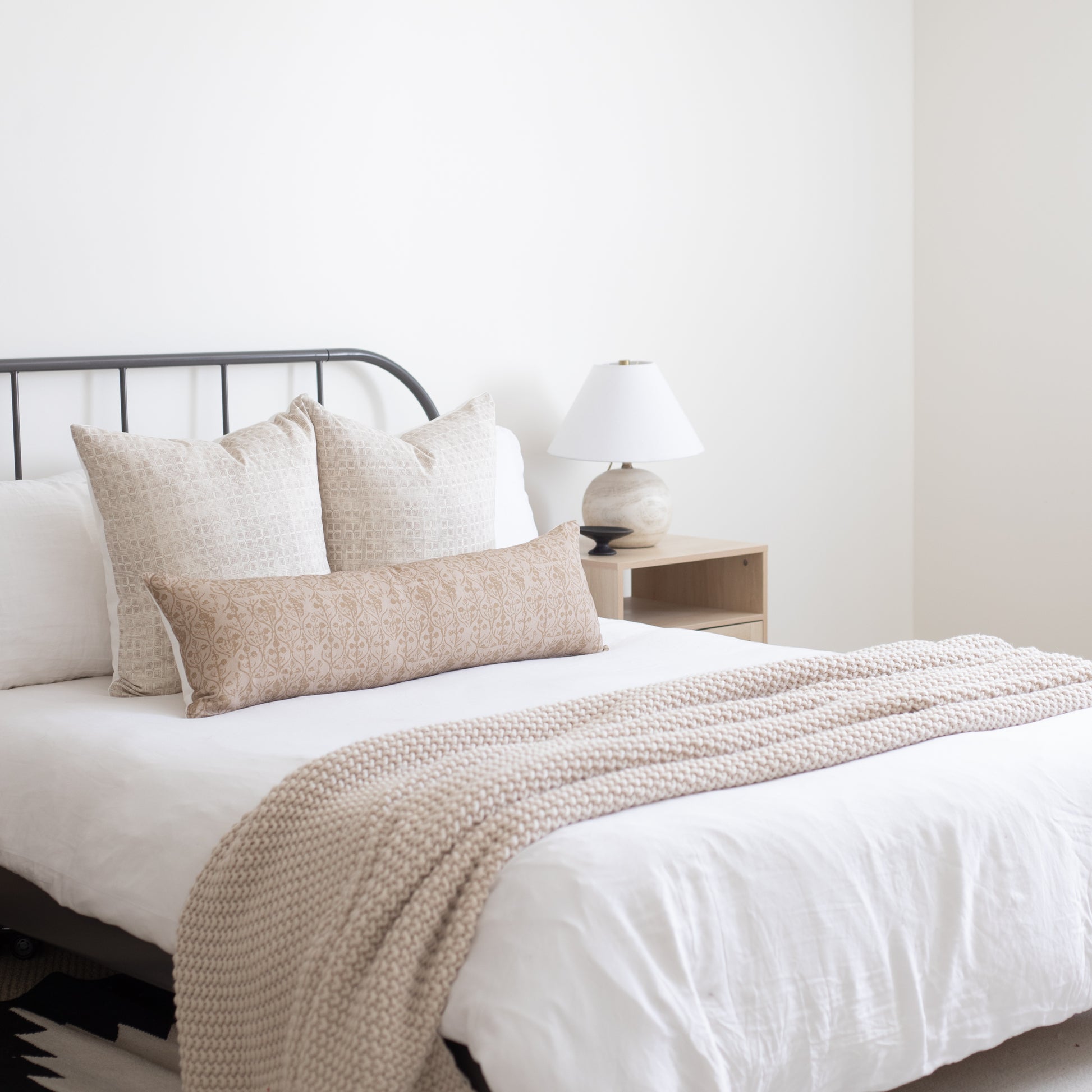 Beige floral patterned throw pillows and matching textured throw blanket arranged on a bed with white bedding.