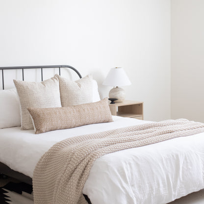 Beige floral patterned throw pillows and matching textured throw blanket arranged on a bed with white bedding.