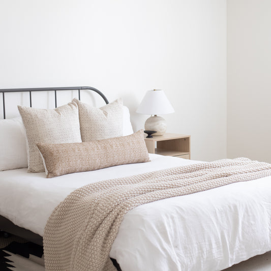 Beige floral patterned throw pillows and matching textured throw blanket arranged on a bed with white bedding.