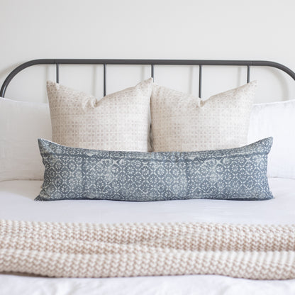 Blue-gray lumbar pillow with diamond floral pattern displayed on bed with neutral pillows.