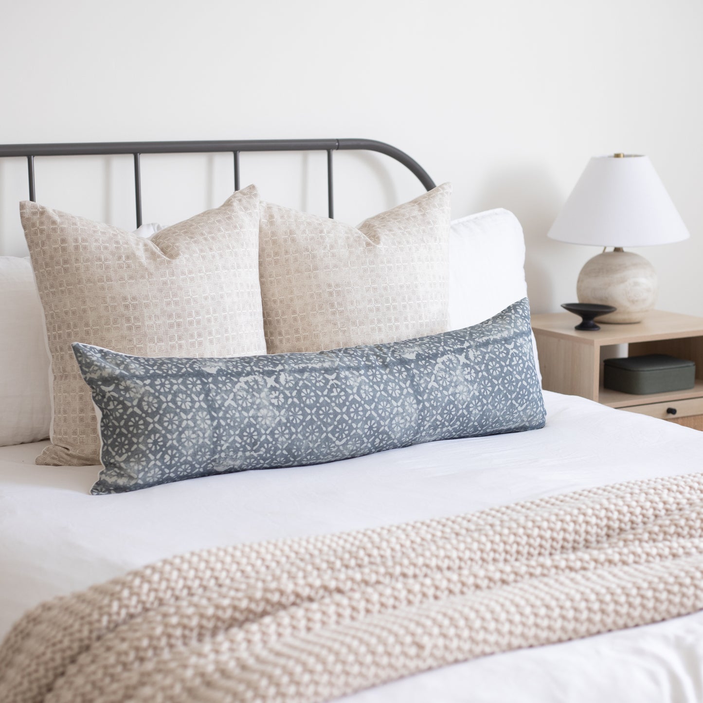 Blue and white diamond floral lumbar pillow displayed on a bed with coordinating neutral pillows.