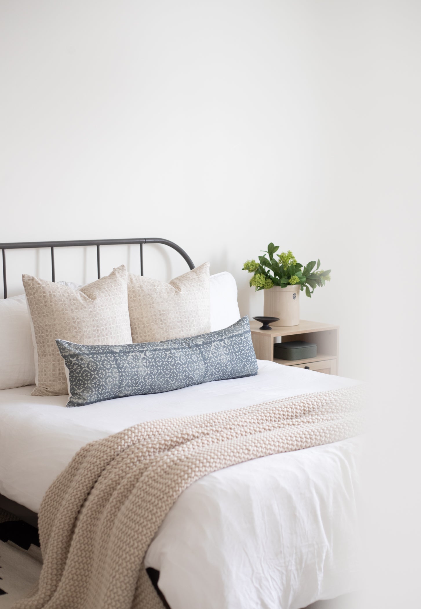 Blue floral lumbar pillow displayed on bed with cream pillows and neutral bedding.