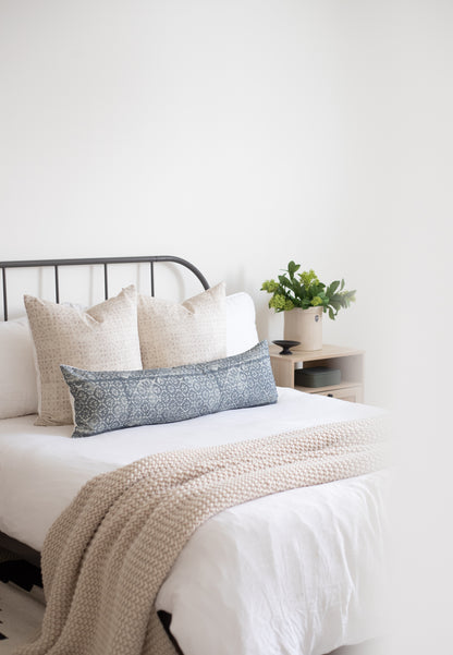 Blue floral lumbar pillow displayed on bed with cream pillows and neutral bedding.