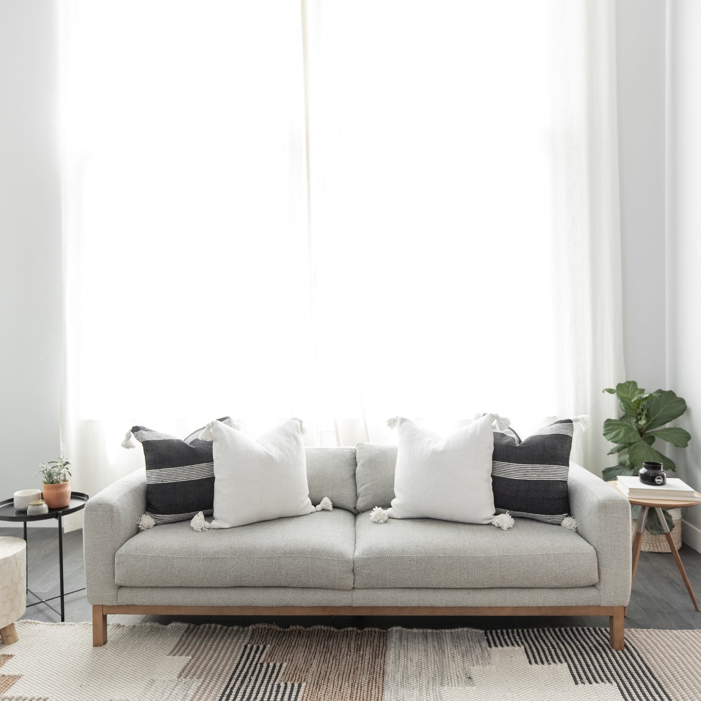Light gray upholstered sofa with wooden legs, decorated with white and black pillows, positioned against a white wall with sh