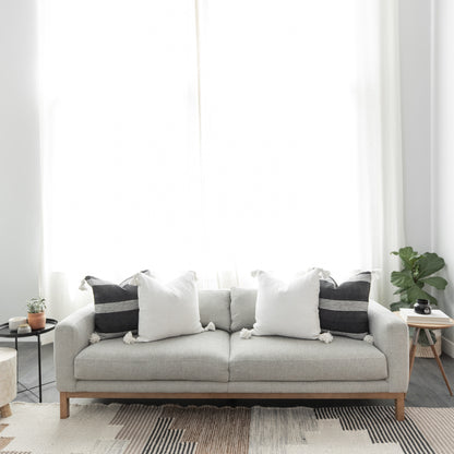 Light gray upholstered sofa with wooden legs, decorated with white and black pillows, positioned against a white wall with sh