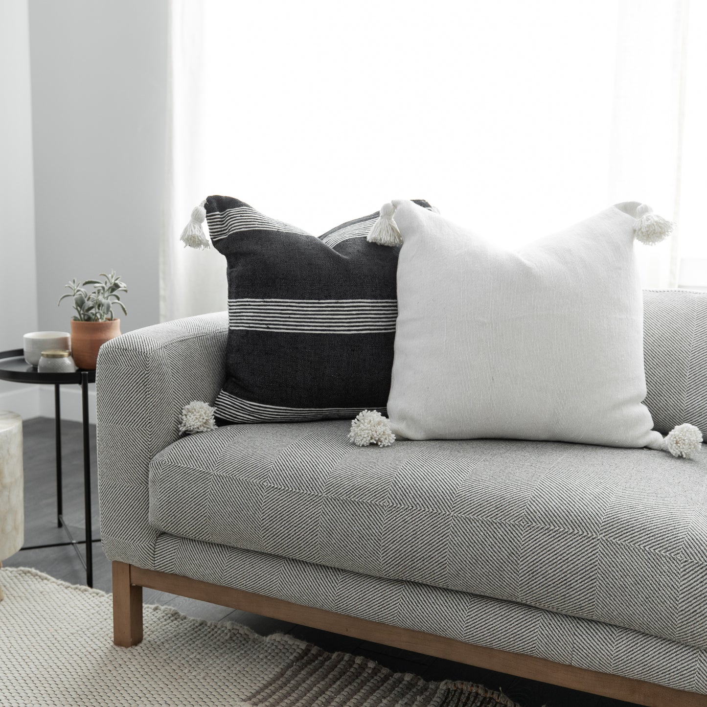 Two decorative pillows with tassels on a gray upholstered sofa: one black with white stripes, one white textured.