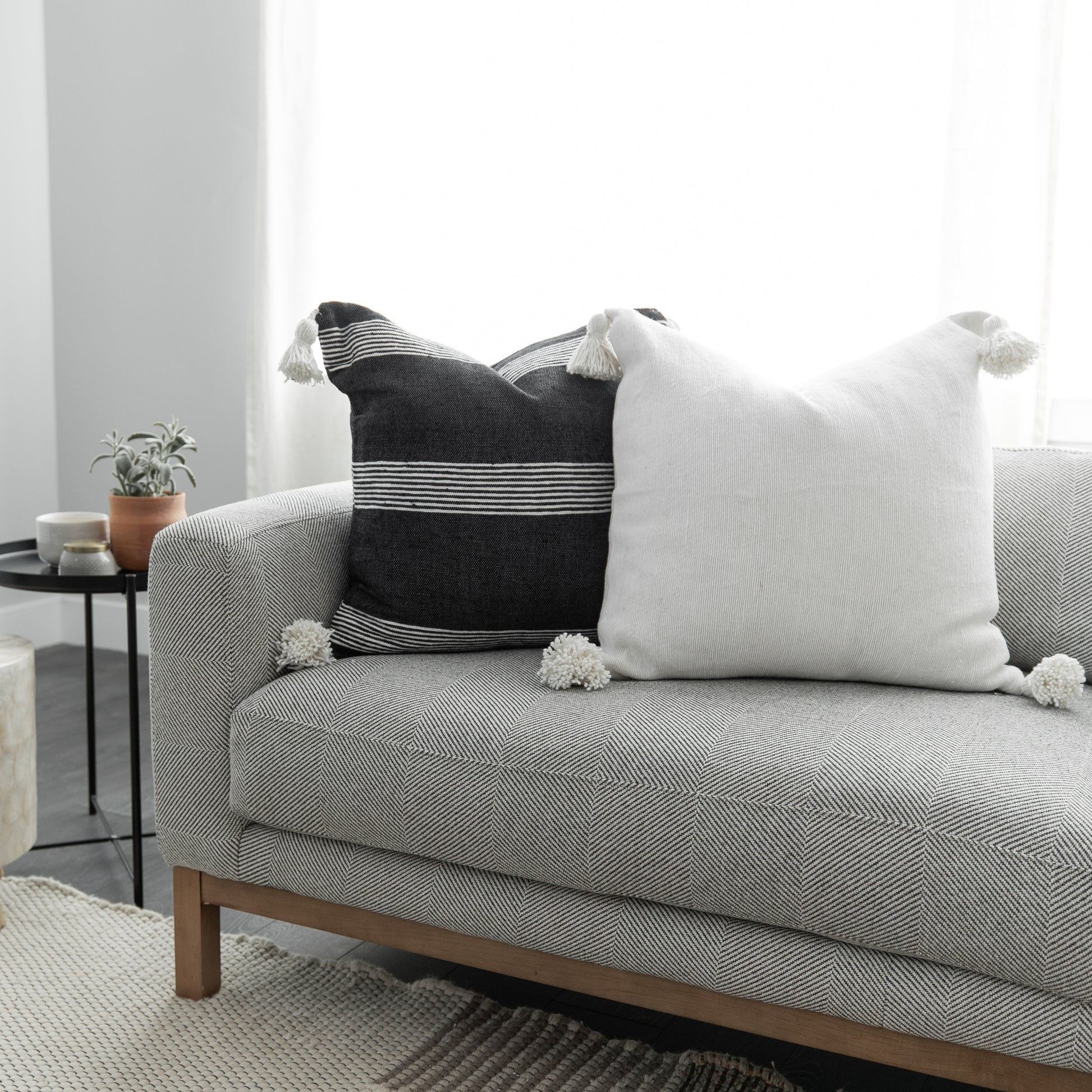 Two decorative pillows with tassels on a gray upholstered sofa: one black with white stripes, one white textured.