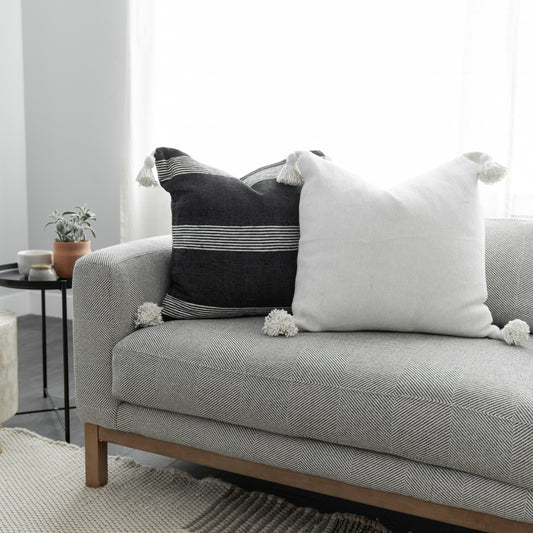 Two decorative pillows with tassels on a gray upholstered sofa: one black with white stripes, one white textured.