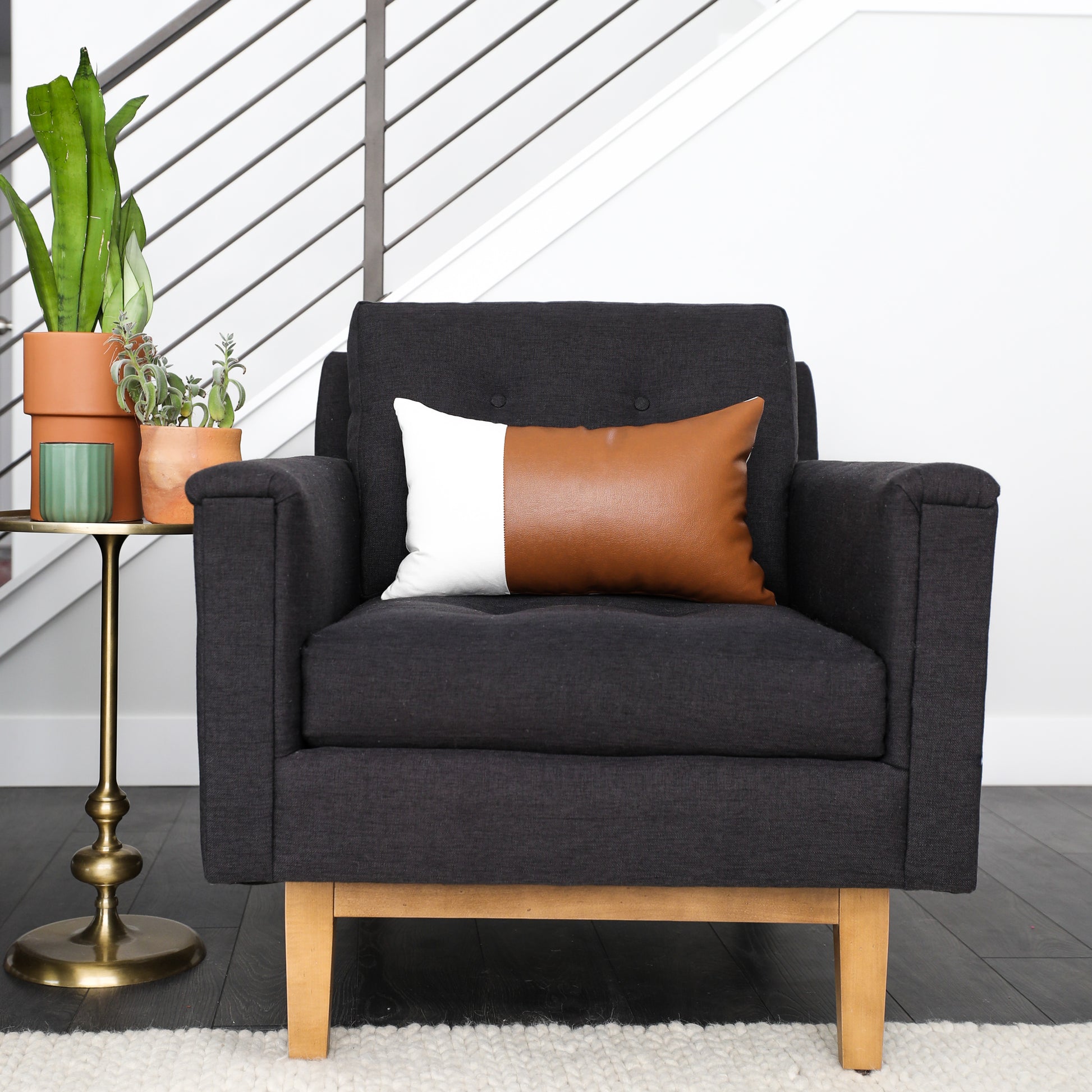 Two rectangular lumbar pillows in cognac leather and cream fabric displayed on a dark gray armchair.
