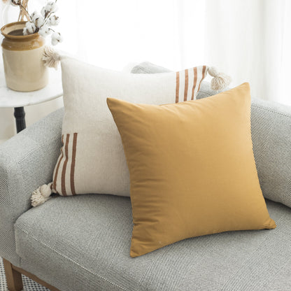 Gold, cream, and striped throw pillows arranged on a gray textured sofa with a decorative vase on a side table.