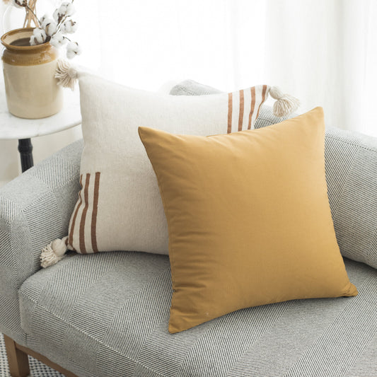Gold, cream, and striped throw pillows arranged on a gray textured sofa with a decorative vase on a side table.