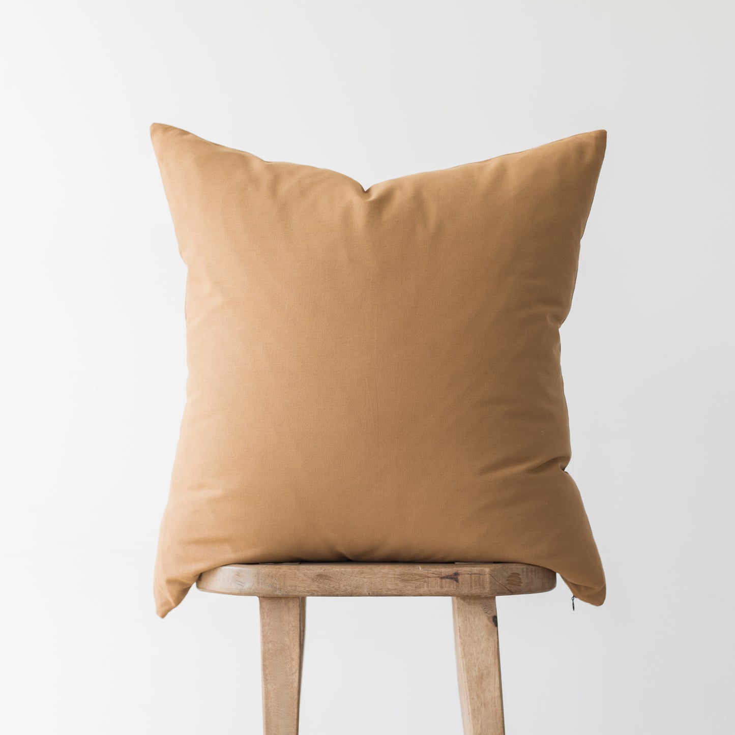 Terracotta-colored square pillow with knife edges resting on wooden stool legs.