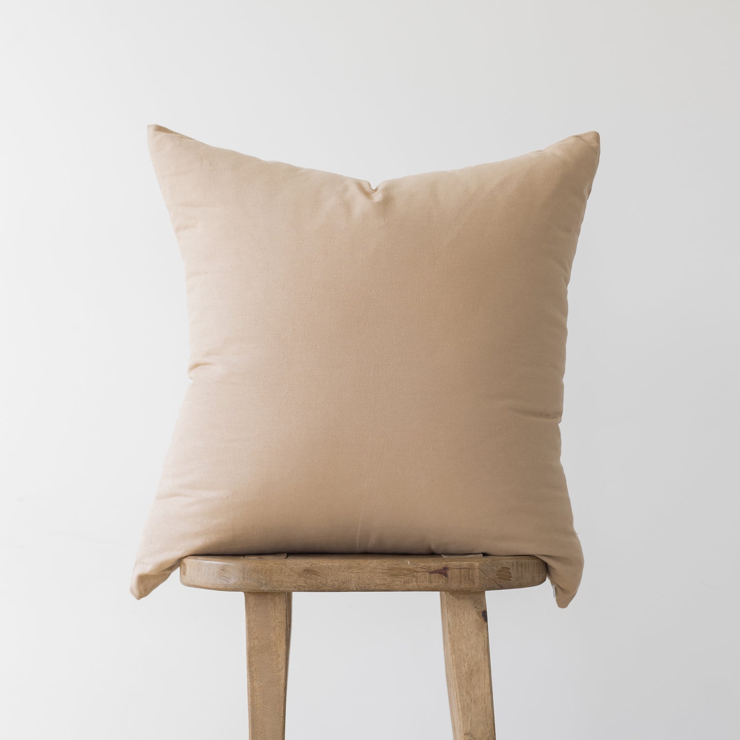 Beige linen pillow cover with envelope closure displayed on wooden stool.